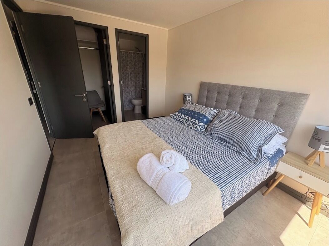 Ein Schlafzimmer mit einem Bett, einem Nachttisch, einer Lampe, einem Handtuch auf dem Bett und einer Tür zu einem Badezimmer.