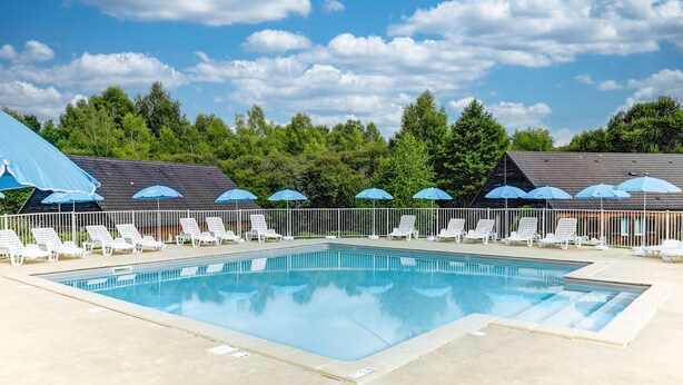 Ein Schwimmbecken mit Liegestühlen und Sonnenschirmen, umgeben von Bäumen und blauem Himmel.