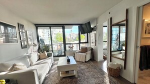 A modern living room with a sofa, coffee table, and a large window with a city view. - 5 minute walk to BC Place | Stylish Apartment | Sleeps 3 (Vancouver)