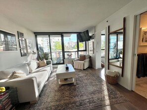 A modern living room with a sofa, coffee table, and a large window with a city view. - 5 minute walk to BC Place | Stylish Apartment | Sleeps 3 (Vancouver)