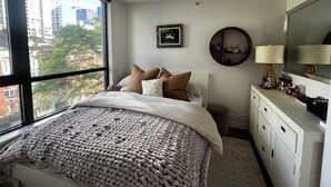 A bedroom with a large window, a bed with a textured blanket, a round mirror, and a dresser. - 5 minute walk to BC Place | Stylish Apartment | Sleeps 3 (Vancouver)