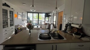 A modern kitchen with a central island, a dining area with a sofa, and a view through large windows. - 5 minute walk to BC Place | Stylish Apartment | Sleeps 3 (Vancouver)