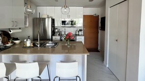 A modern kitchen with stainless steel appliances, a central island with bar stools, and a wooden door. - 5 minute walk to BC Place | Stylish Apartment | Sleeps 3 (Vancouver)