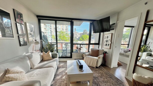 A living room with a sofa, armchair, coffee table, and large windows with a city view. - 5 minute walk to BC Place | Stylish Apartment | Sleeps 3 (Vancouver)