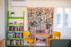 A room with a bookshelf, two chairs, a table, a wall tapestry, and a window. - City cottage oasis with sunken fire pit and private gated driveway parking. (Auckland)
