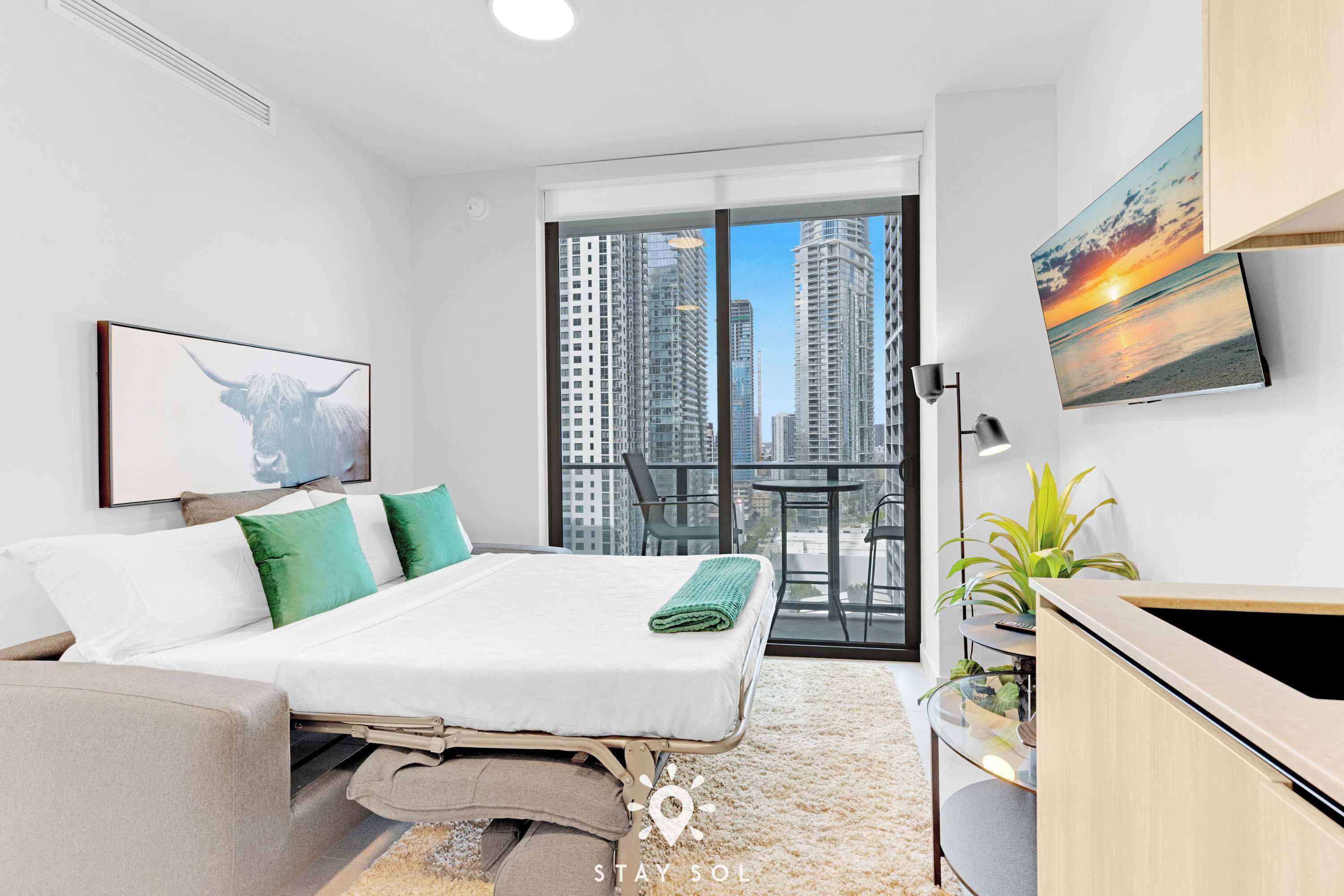 Una moderna camera d'hotel con un letto, una scrivania, una sedia, una TV e un balcone con vista sulla città.