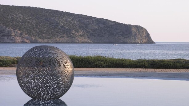 A spherical sculpture on a tiled surface with a coastal view in the background. - Elies Resort (Sifnos)
