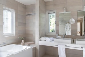 Een moderne badkamer met een bad, twee wastafels, een grote spiegel en een douchehoek.
