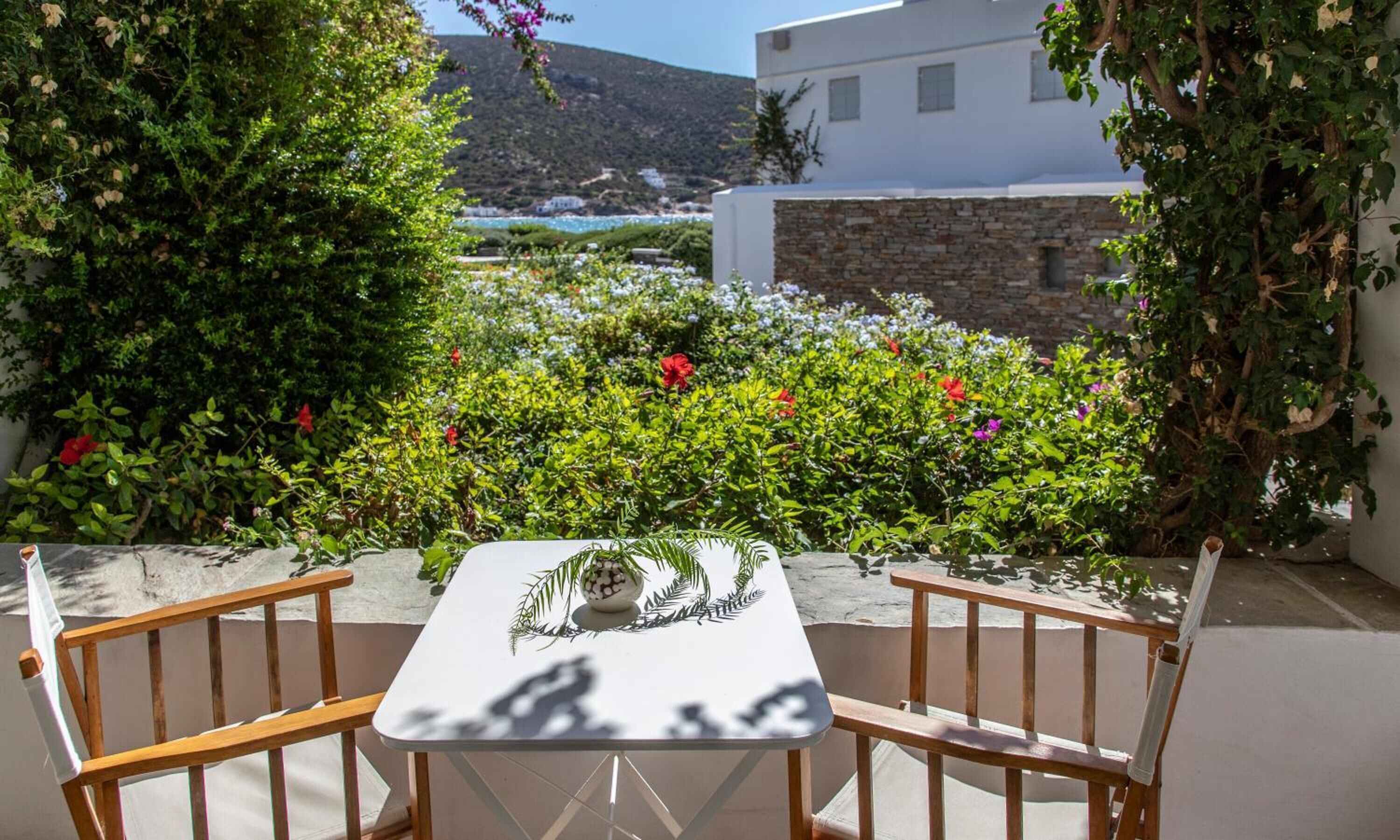 A table with chairs in a garden with a view of a white building and a mountain.