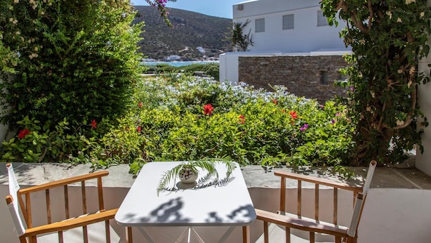 A table with chairs in a garden with a view of a white building and a mountain. - Elies Resort (Sifnos)