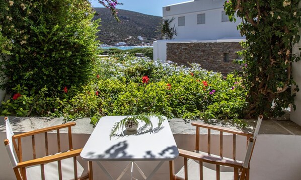 A table with chairs in a garden with a view of a white building and a mountain. - Elies Resort (Sifnos)