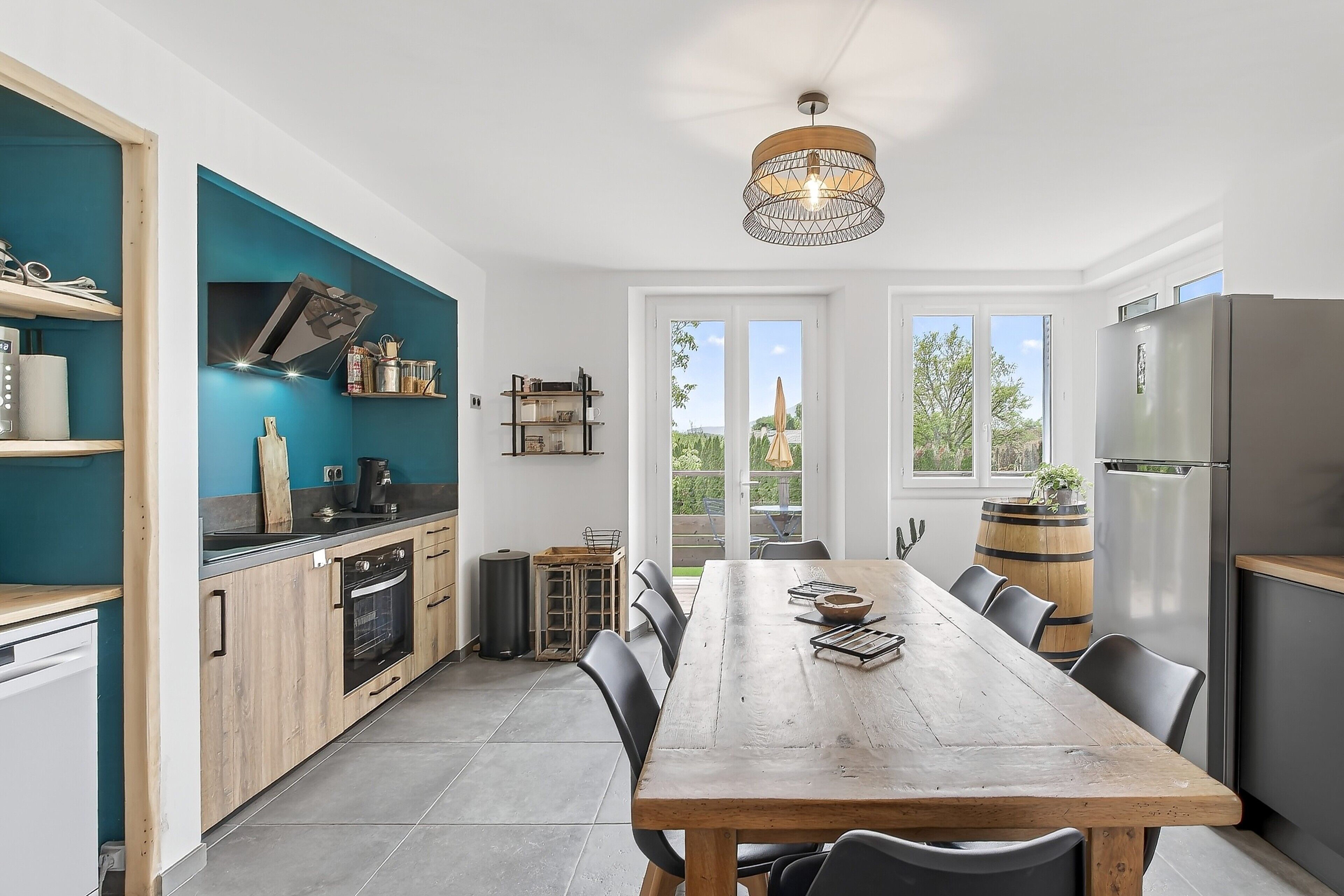 A modern kitchen with a wooden table, black chairs, and a view through large windows.