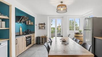 A modern kitchen with a wooden table, black chairs, and a view through large windows.
