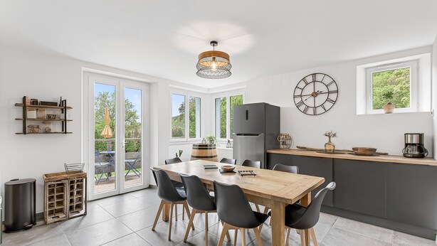 Een moderne keuken met een eethoek, grote ramen en een klok aan de muur.