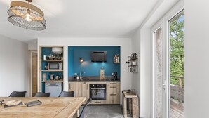 Een moderne keuken met een blauwe accentmuur, houten keukenkastjes, een eethoek met een houten tafel en een grote schuifpui naar buiten.