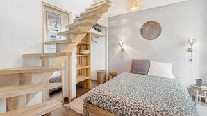 Een slaapkamer met een bed, een houten trap, een wandlamp en een poster.