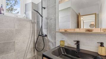 Une salle de bain avec une douche, un lavabo, un miroir et une fenêtre.