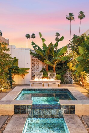 A swimming pool with mosaic tiles, surrounded by tropical plants and a white fence. - Palm Desert Mid-Century Modern | Private Spa, Pool, Piano & Walk to El Paseo (Palm Desert)