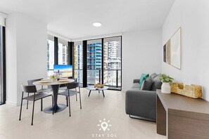 A modern living room with a dining area, large windows, and a view of high-rise buildings. - Resort Living & Peaceful Balcony Mornings – 1BR (Miami)
