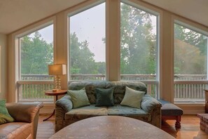 A room with a large window, a sofa, a table, and a lamp. - Winter Escape | Sauna, Fireplace, Games (Parry Sound)