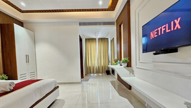 A modern hotel room with a bed, wardrobe, vanity, and a TV displaying 'NETFLIX'. - TrueLife SRB Suites (Tirupati)