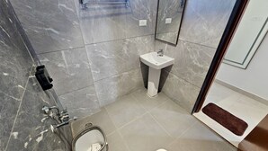 A bathroom with a marble floor, a white sink, a towel rack, and a shower with a handheld showerhead. - TrueLife SRB Suites (Tirupati)