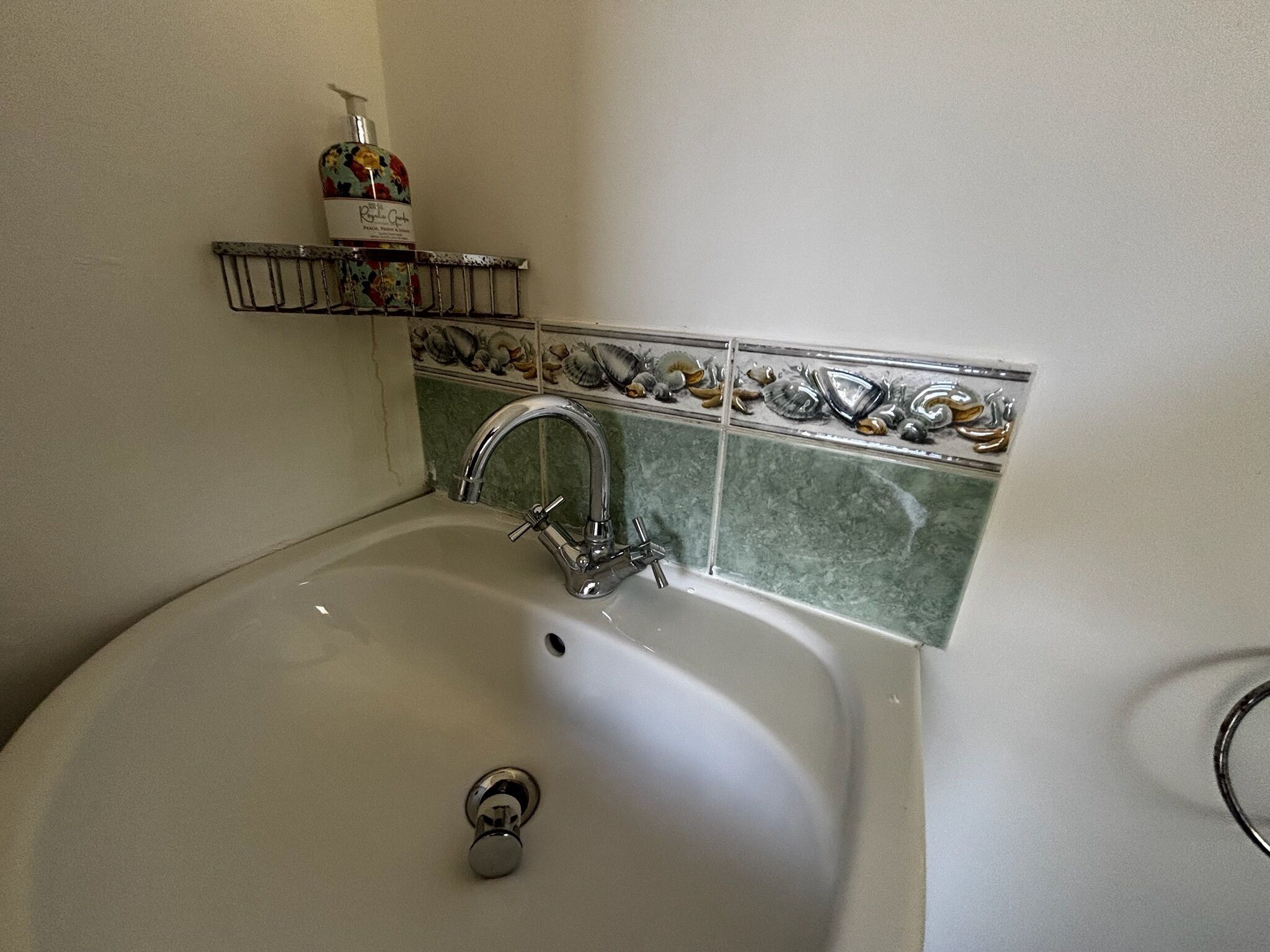 A bathroom with a white sink, a chrome faucet, and a shelf with toiletries.