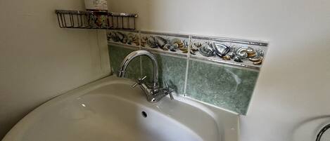 A bathroom with a white sink, a chrome faucet, and a shelf with toiletries.