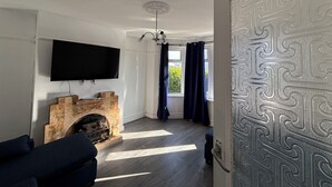 A living room with a flat-screen TV, a fireplace, a sofa, and a view through a window with curtains. - Tranquil Hideaway w/Hot Tub and Pool Table (Cardiff)