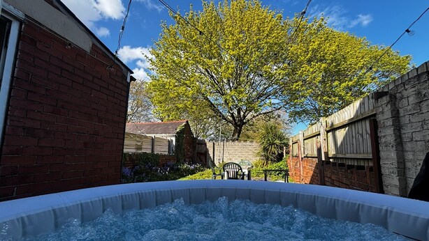 A hot tub in a backyard with a brick wall, a wooden fence, and a tree. - Tranquil Hideaway w/Hot Tub and Pool Table (Cardiff)