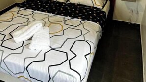 Ein Bett mit einem geometrisch gemusterten Überwurf, zwei Kissen und einem Holzkopfbrett.