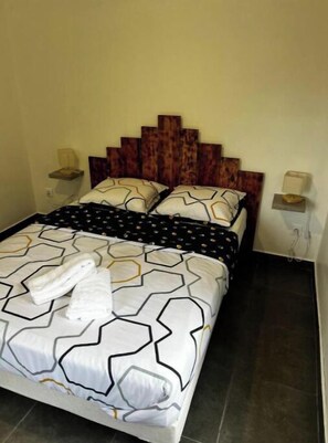 Ein Bett mit einem geometrisch gemusterten Überwurf, zwei Kissen und einem Holzkopfbrett.