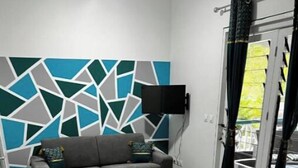Ein Zimmer mit grauem Sofa, einem geometrischen Wandmuster und einem Fliesenboden.