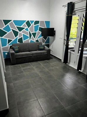 Ein Zimmer mit grauem Sofa, einem geometrischen Wandmuster und einem Fliesenboden.