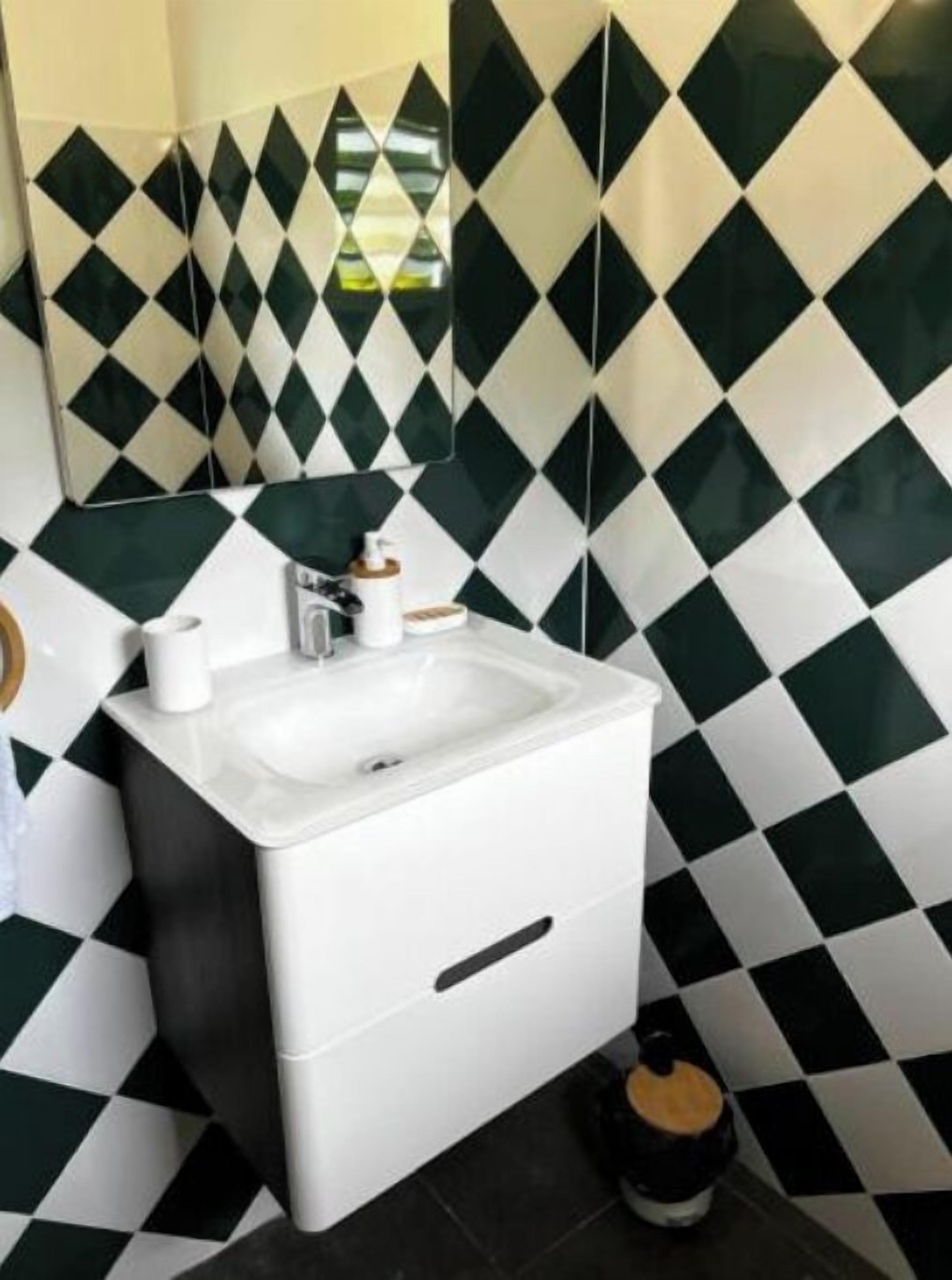Une salle de bain avec un lavabo blanc, un miroir et un pare-feu en carreaux noirs et blancs.