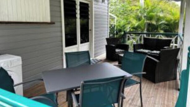 Eine überdachte Terrasse mit Tisch und Stühlen, einer Tür und Blick ins Grüne.