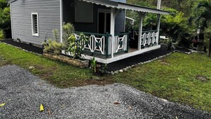 Ein kleines, eingeschossiges Haus mit Veranda, umgeben von Grün und einer Schotterzufahrt.