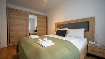 Une chambre d’hôtel avec un lit, une armoire en bois, une table de chevet avec une lampe et un ventilateur de plafond.
