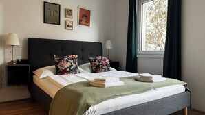 Een opgemaakt bed met bloemenkussens, een bedlampje en een ingelijste foto aan de muur.