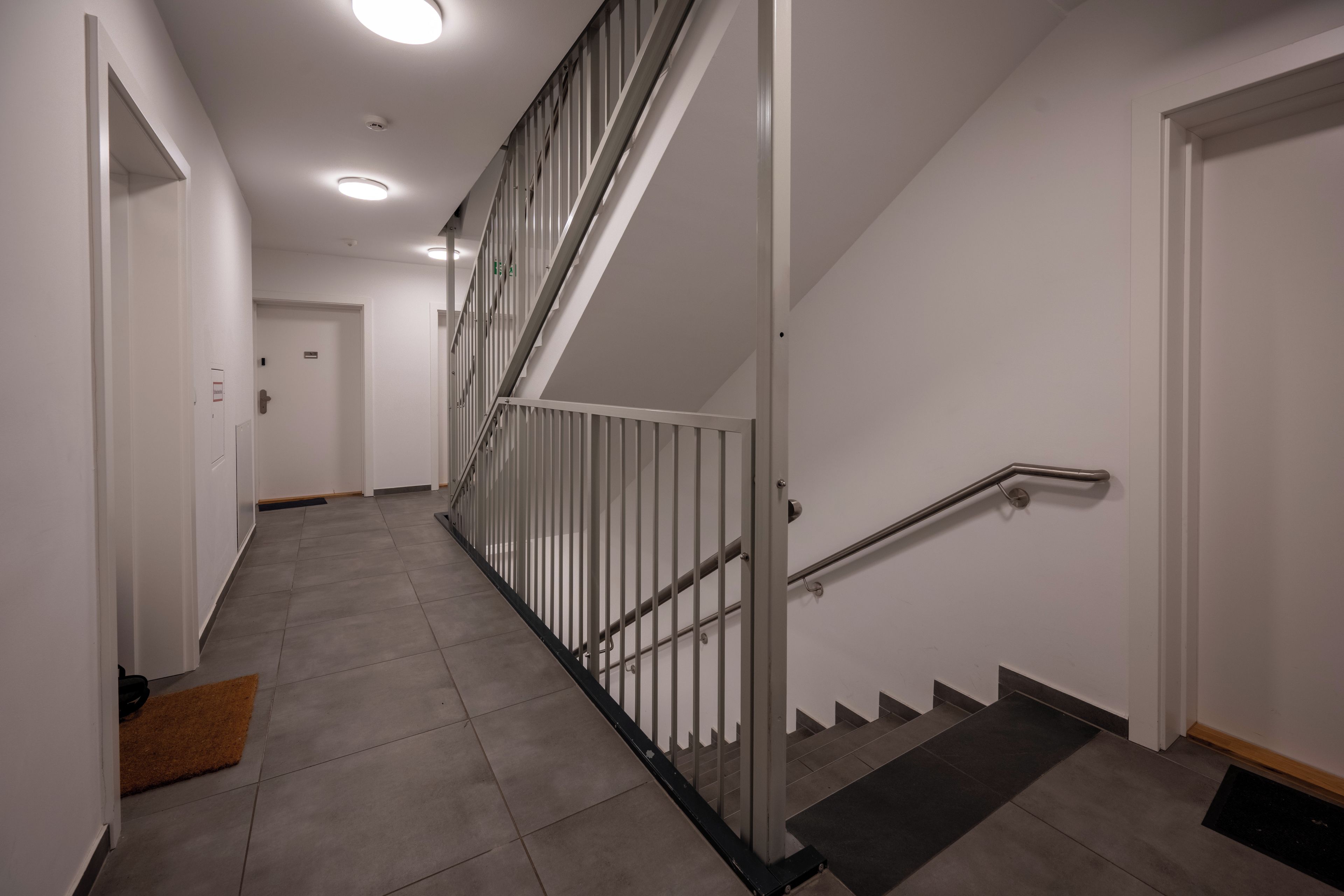 Een moderne trap met metalen leuning en handrail, die leidt naar een deur met een bord erboven.