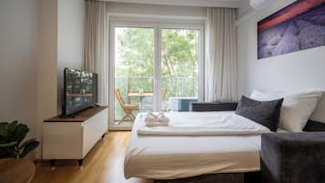 A modern hotel room with a bed, a TV, a small table, and a chair by the window.