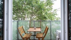 A balcony with a wooden table and chairs, a mesh fence, and a view of trees. - Moderne & ruhige Apartments in Wien (Vienna)