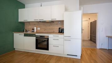 Een kleine keuken met witte kastjes, een inbouwoven en een houten spatwand.