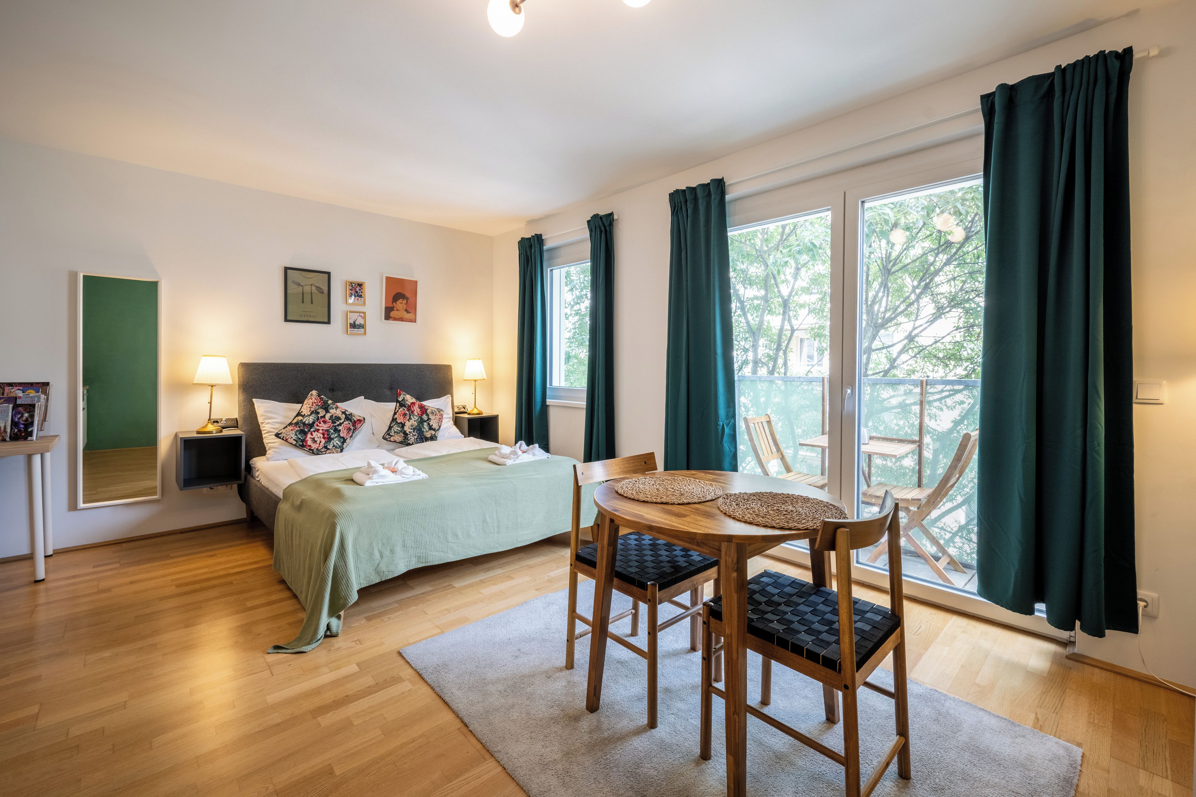 Hotelkamer met een bed, twee nachtkastjes, een bureau, een stoel, een balkon met gordijnen en een raam met uitzicht op bomen.