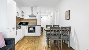 Een moderne keuken met witte kasten, een magnetron, een oven en een houten aanrecht. Er is een eethoek met een tafel en stoelen.