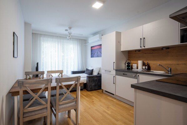 A modern kitchen with a dining area, wooden flooring, and a view of a garden through the window. - Moderne & ruhige Apartments in Wien (Vienna)