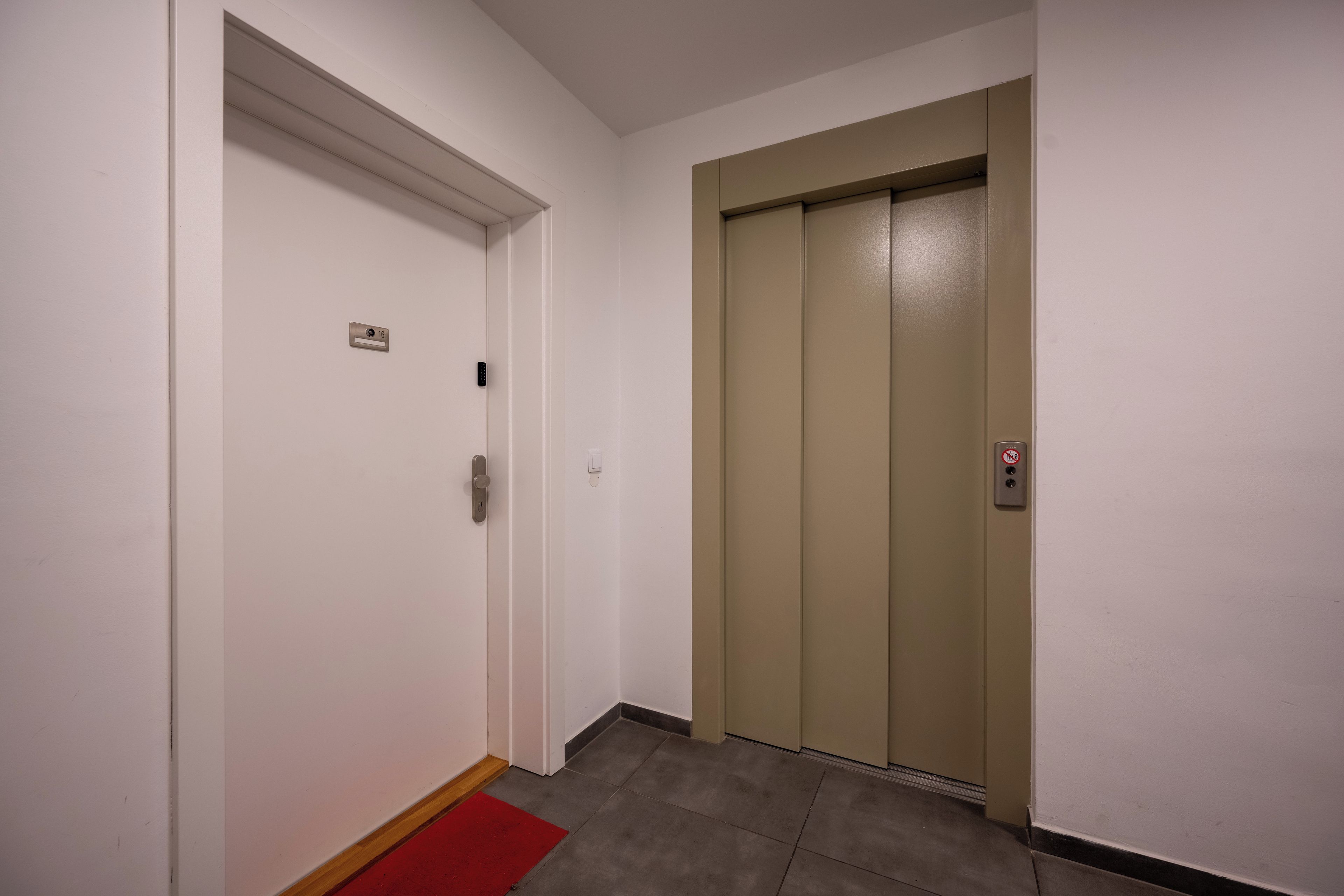 A hallway with a white door and a beige elevator.