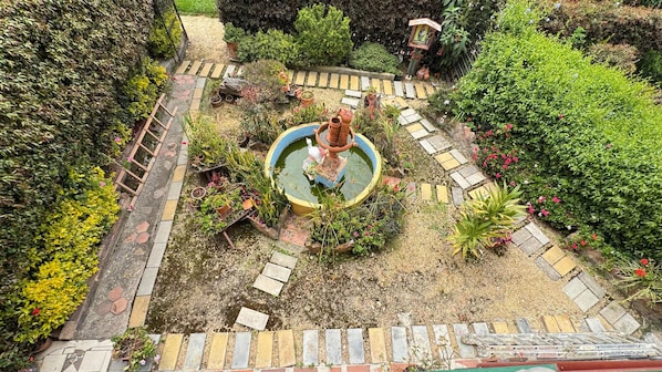 A garden with a central fountain, stone pathways, and various potted plants.
