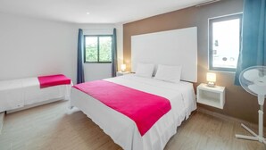 Quarto de hotel com uma cama grande, mesas de cabeceira, um ventilador e uma janela com cortinas.