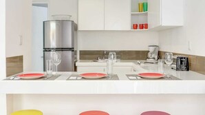 A modern kitchen with white cabinets, a stainless steel refrigerator, a coffee maker, and a toaster. There are three stools in red, orange, and yellow. - Rooftop, 2nd Floor, Air, King Bed, V12 (Playa del Carmen - Valentina Suites)
